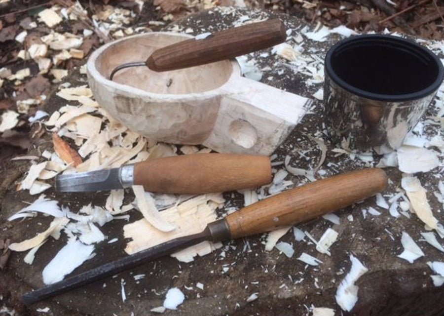 Houtsnijgereedschap en een half gesneden houten mok tussen de houtkrullen