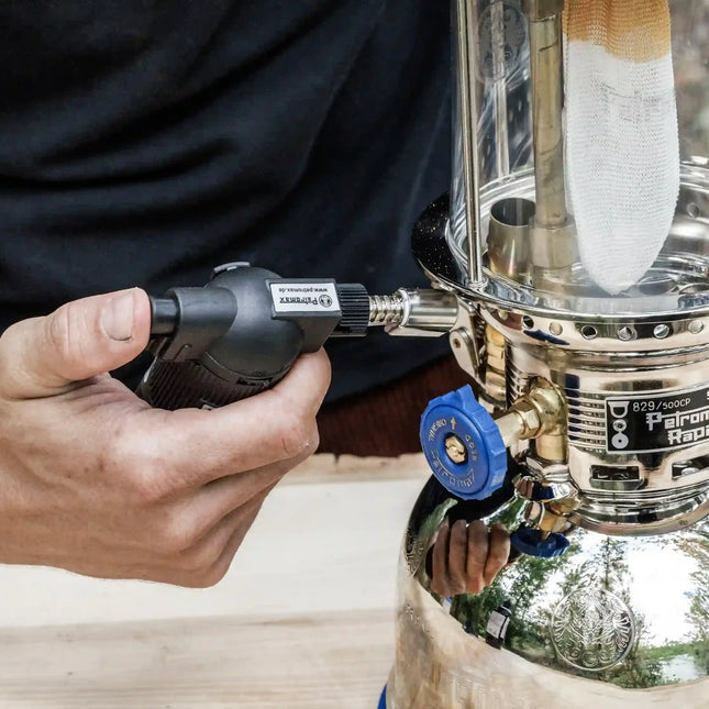 Carburateur van een Petromax HK500 voorverwarmen met een gasbrander, met de gloeikous zichtbaar achter het glas