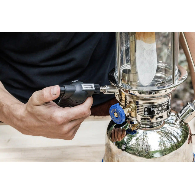 Carburateur van een Petromax HK500 voorverwarmen met een gasbrander, met de gloeikous zichtbaar achter het glas