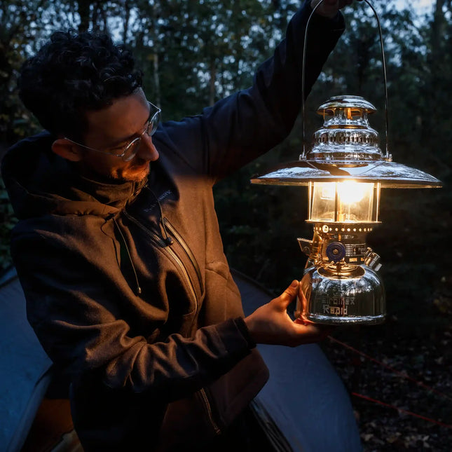 Man houdt een brandende Petromax HK500 met reflectorkap omhoog bij een tent in het bos