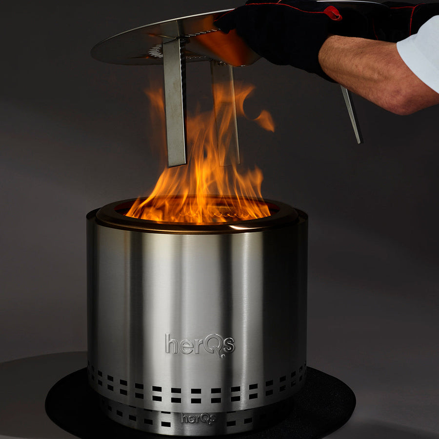 Hand met BBQ-handschoen plaatst herQs Heater Blaze warmteverspreider op brandende Blaze vuurkorf