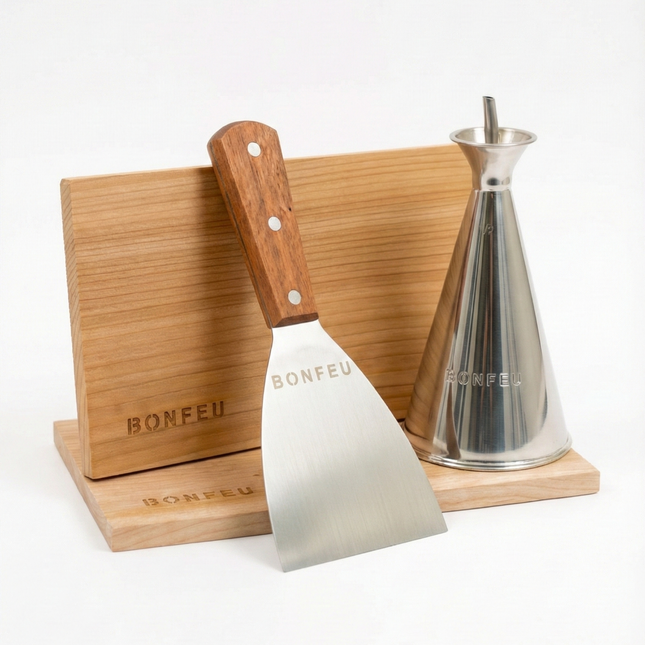 BonFeu kookset: RVS spatel met houten handvat en conische RVS oliekan gepresenteerd op cederhouten rookplankjes met BonFeu logo